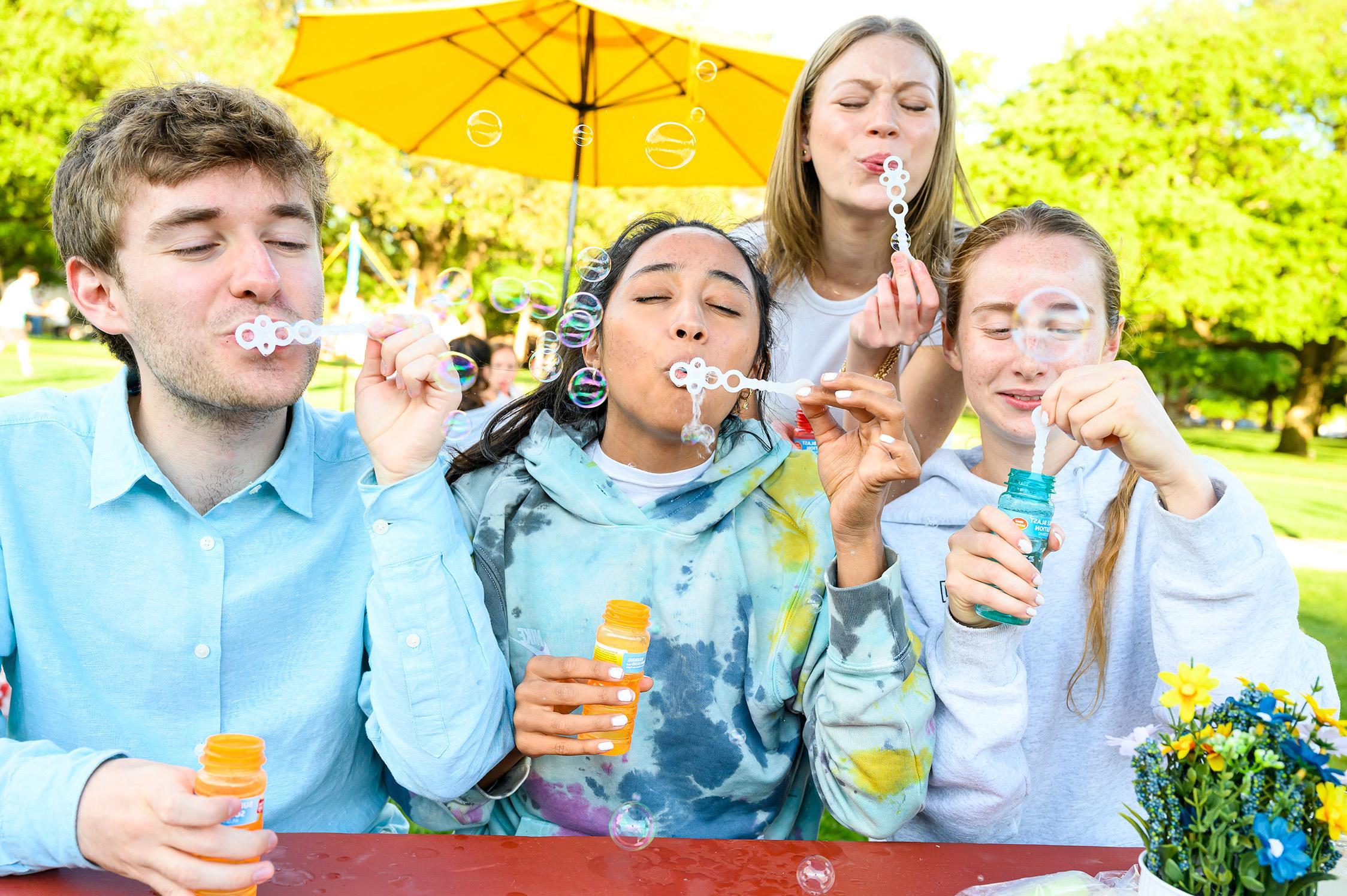 four students blowing bubbles outside